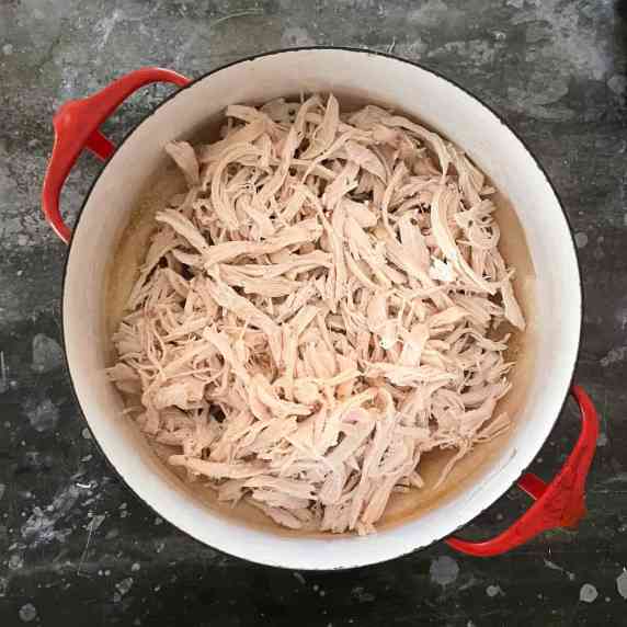 shredded chicken in a red dutch oven on a dark grey counter.