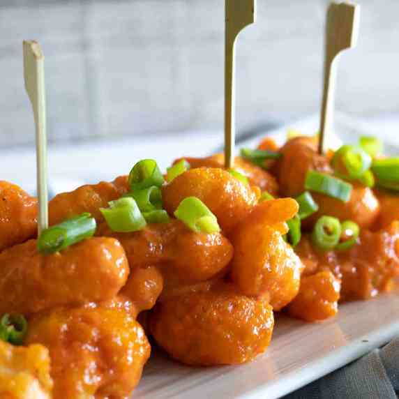 Dynamite shrimp with skewered served on a white plate topped with scallions.