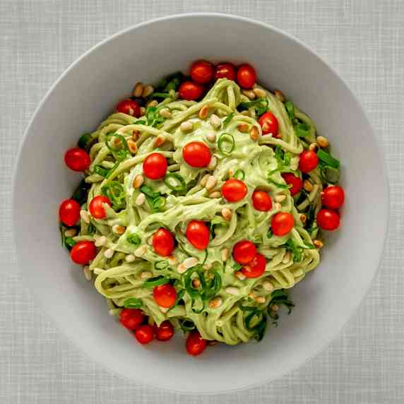 A plate with spaghetti with an easy, vegan and creamy avocado sauce, topped with tiny cherry tomatoe