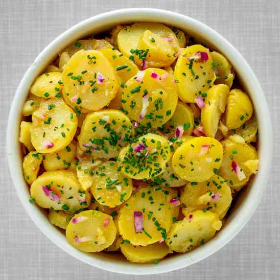 A bowl loaded with potato salad, garnished with finely chopped chives