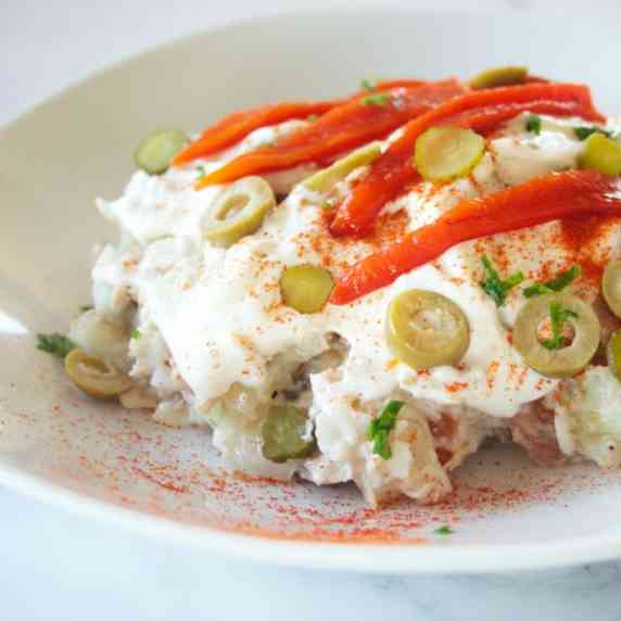 a shallow bowl of ensalada rusa sits garnished with paprika, olives, chives, and roasted pepper