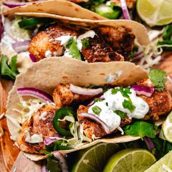 Fish tacos with sour cream and lime wedges.