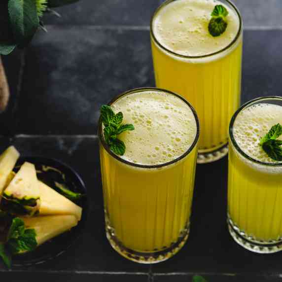three tall glasses are filled with pineapple juice and garnished with mint leaves. 