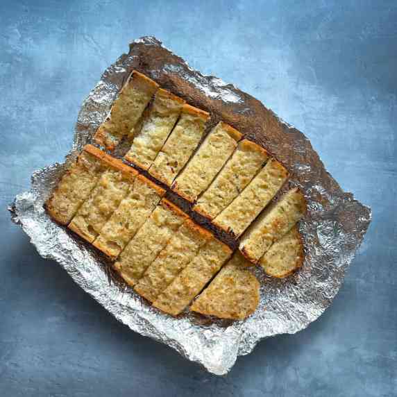 slices of garlic bread wrapped in aluminum foil on a blue background.