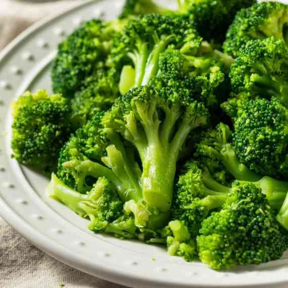 Close view of steamed broccoli tossed in garlic butter on a white plate.