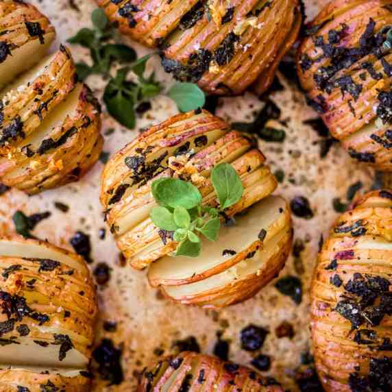 Overhead view of hasselback potatoes decorated with green herbs on baking sheet.