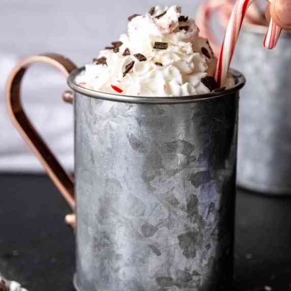 A mini candy cane is tucked into the whipped cream topping on a peppermint mocha in a metal mug.