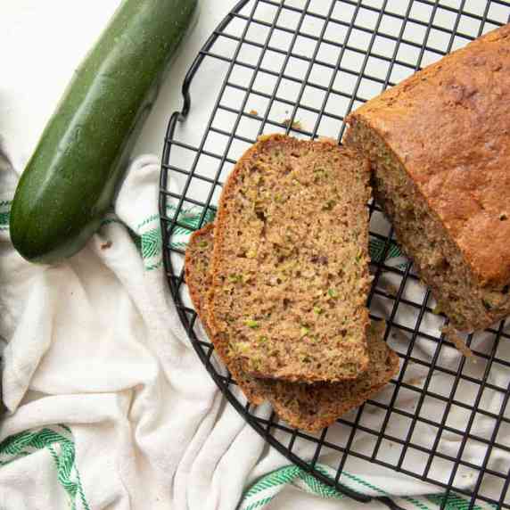Loaf of gluten-free zucchini bread on a cooling rack with two slices cut and stacked beside it.