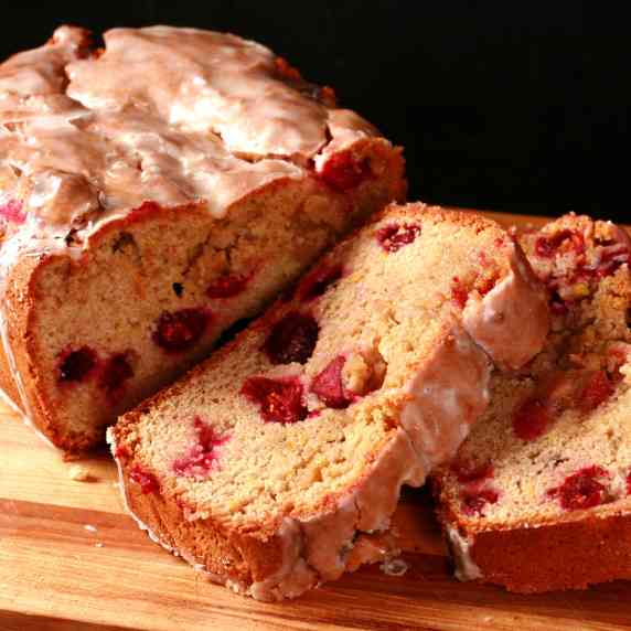 A sliced loaf of gluten free cranberry orange bread on a wooden cutting board.