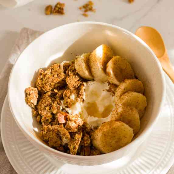Greek yogurt with granola clusters, banana slices and honey in a white bowl.