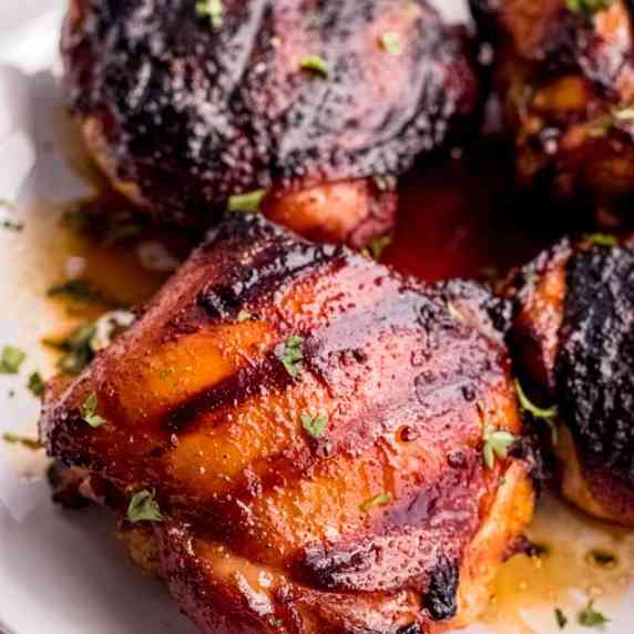 Close view of marinated, grilled chicken thighs on a white plate with flavorful juices.