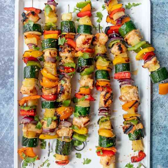 Grilled chicken and veggie skewers arranged on a white serving platter, sprinkled with fresh herbs.
