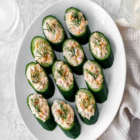 Slices of cucumber topped with creamy crab arranged on a white oval platter on a grey countertop. 