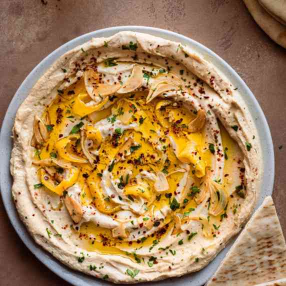 Hummus in a large shallow plate with garlic, lemon and olive oil on top.