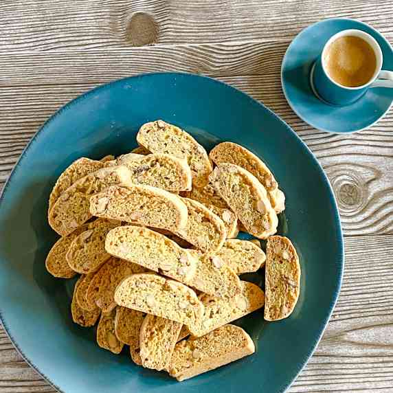 Mini almond biscotti piled on a blue plate on a woodgrain surface.