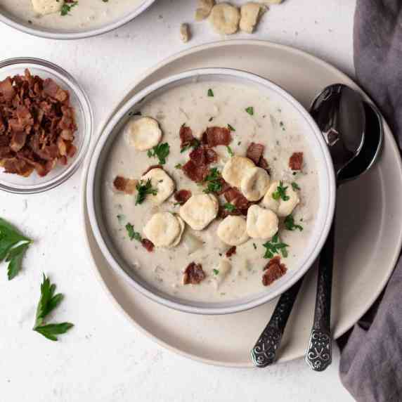 Clam chowder in a soup bowl garnished with bacon, parsley, and oyster crackers.