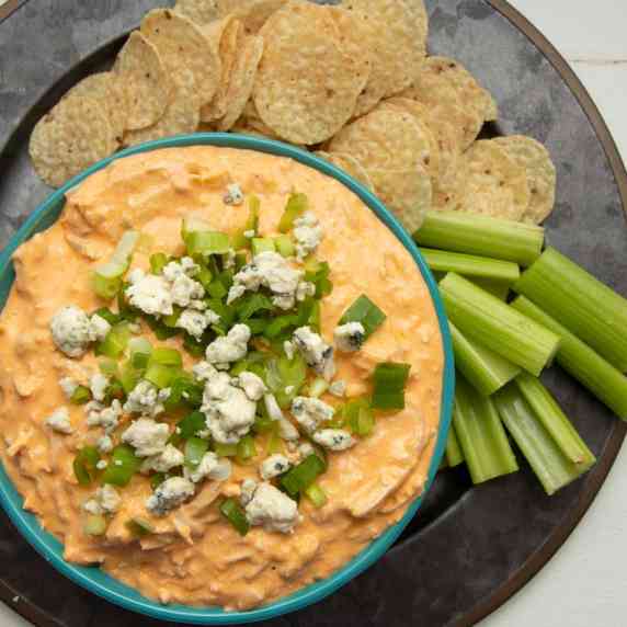 Bowl of Instant Pot buffalo chicken dip surrounded by tortilla chips and celery sticks on a platter.