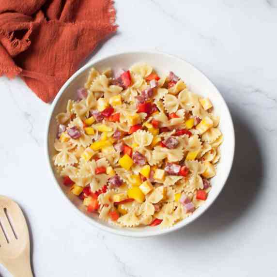 pasta salad (bow tie pasta, cheese cubes, bell pepper, salami, and ham pieces) in a white bowl. 