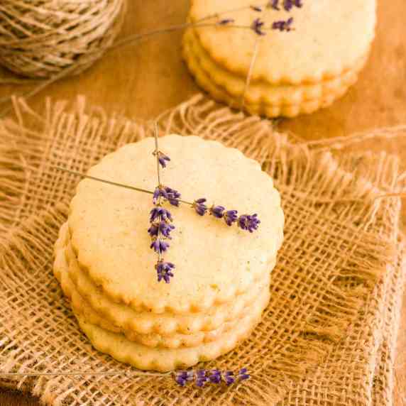 Stacks of lemon lavender cookies on burlap with lavender flowers.