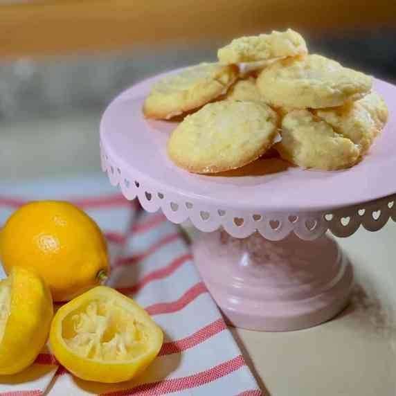 Lemon shortbread piled on a pink cake stand with lemons on a towel.