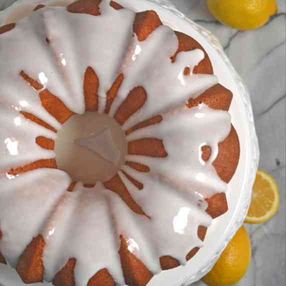 Lemon Bundt Cake on a white cake stand with lemons beside it.