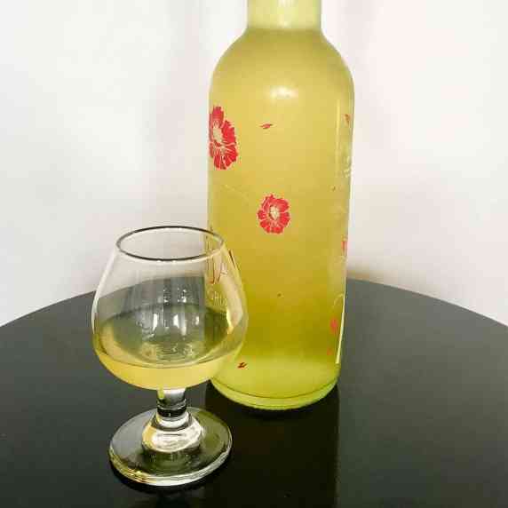 Homemade limoncello in a bottle and glass on a black table.