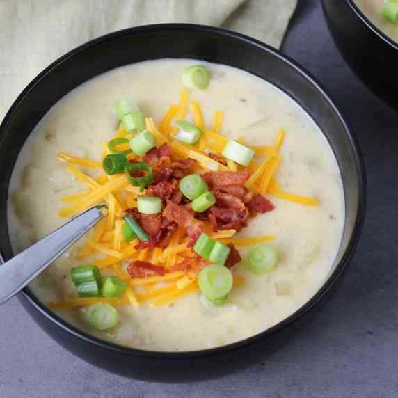 A bowl of creamy potato soup loaded with bacon bits, cheddar cheese, and scallions.