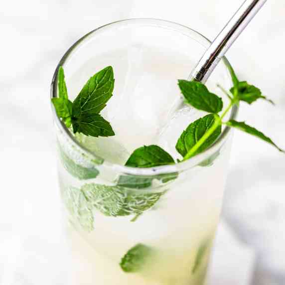 A lychee mojito garnished with fresh mint leaves, on a white marble table.