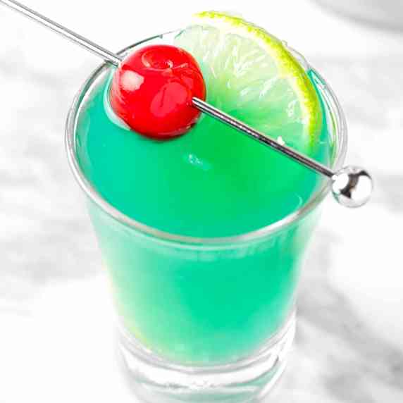 A malibu rum shooter garnished with a maraschino cherry and lime slice. 