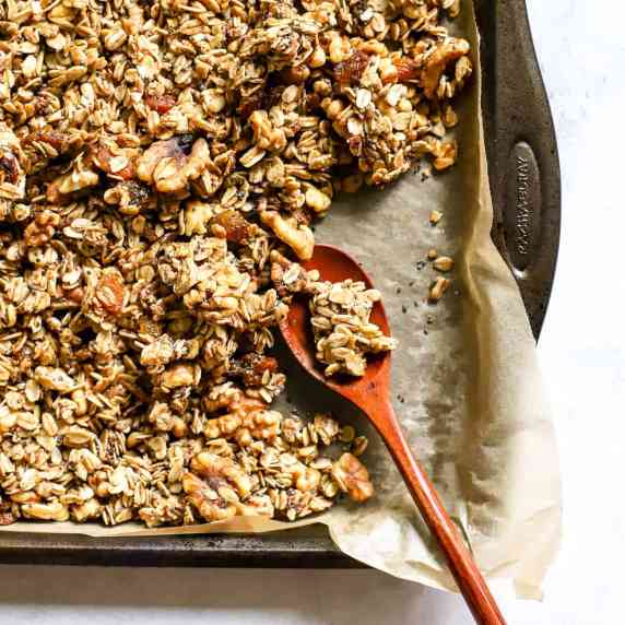 Maple cinnamon walnut granola on parchment-lined sheet pan with wooden spoon