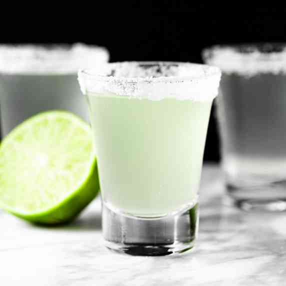 Three margarita shooters with a salted rim, on a black background.