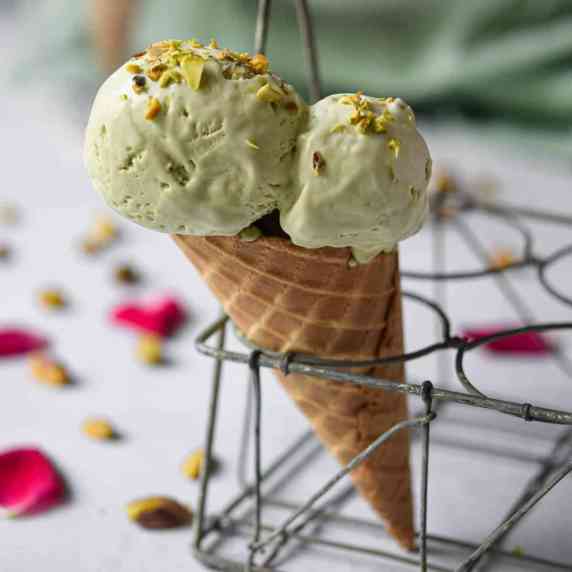 Pistachio ice cream in a cone in a wire holder.