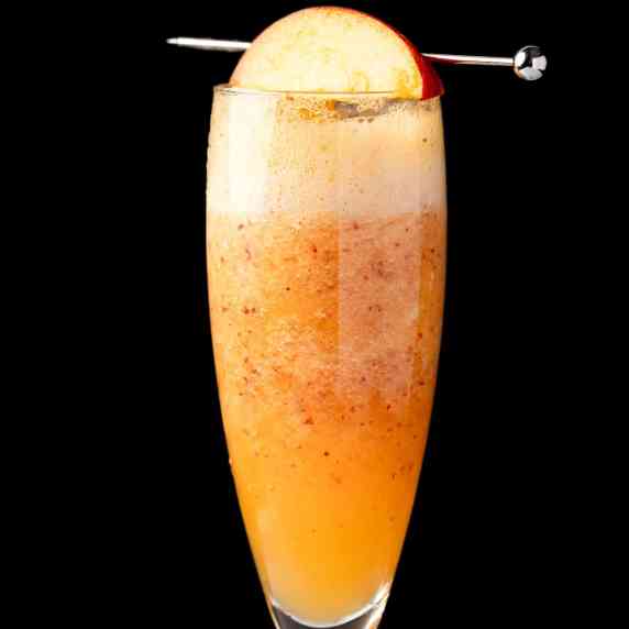 A non alcoholic peach bellini garnished with a peach slice, on a black background.