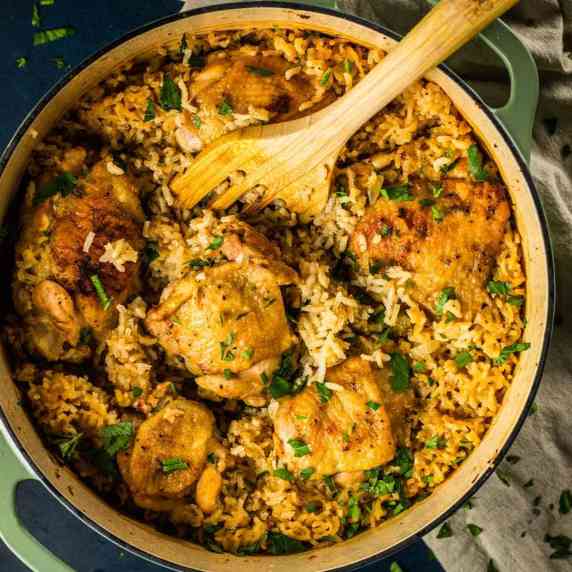 round dutch oven pot with crispy chicken thighs and rice with wooden spatula scooping it out