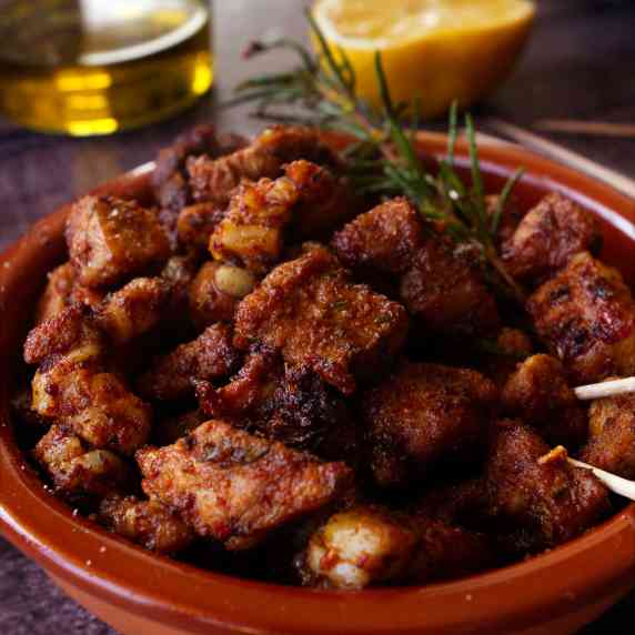 a  small tapas serving of paprika-infused pork bites sits beside a sherry and lemon