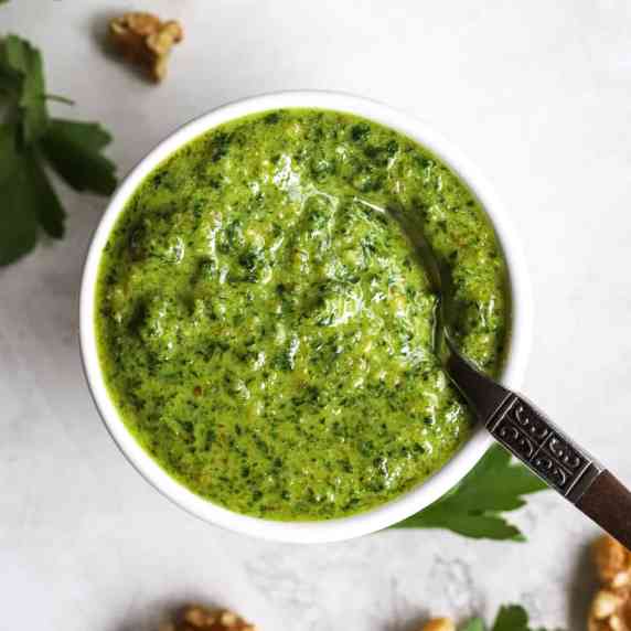 Parsley walnut pesto in small white bowl with spoon, on white and light gray surface
