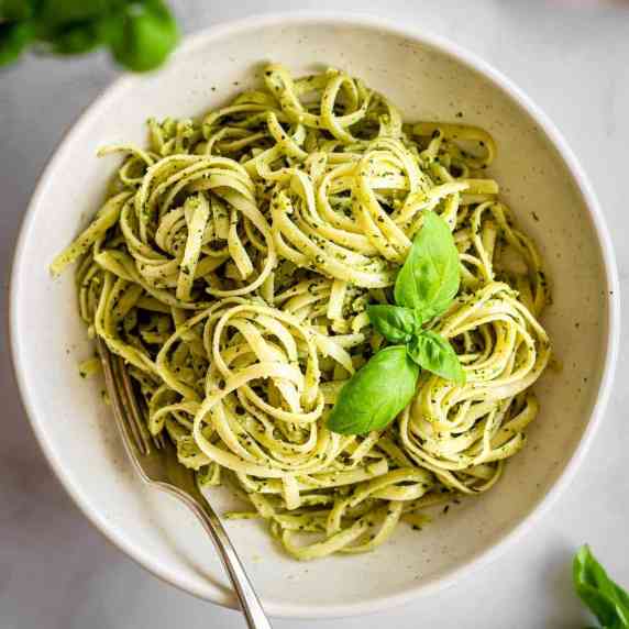 White bowl of pasta al pesto by Vancouver with Love, decorated with basil leaves.