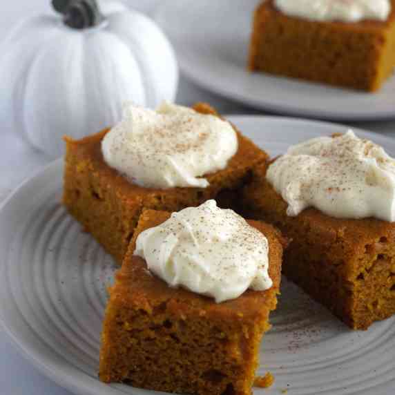 Three pumpkin bars on a plate with a white pumpkin in the background.