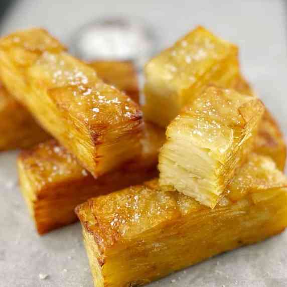 slices of golden brown potato pave on parchment paper on a baking tray with flakey salt.