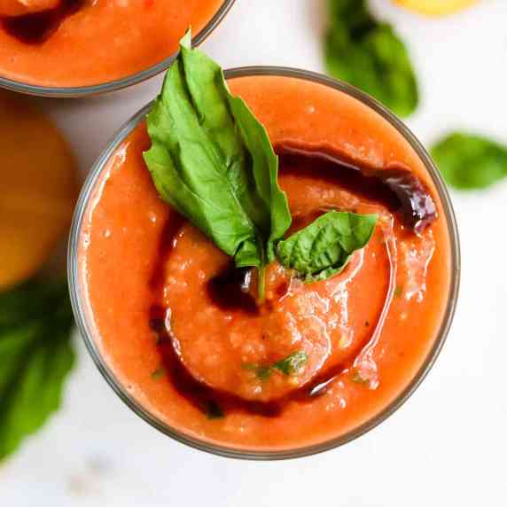 Peach basil gazpacho in glass with fresh basil leaf garnish and swirl of balsamic glaze