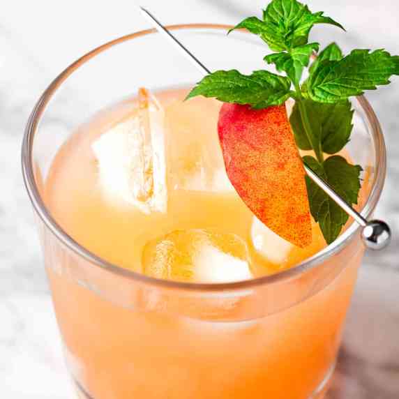 A peach on the beach cocktail garnished with a slice of peach.