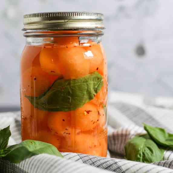 Pickled cantaloupe balls in a mason jar with basil leaves.