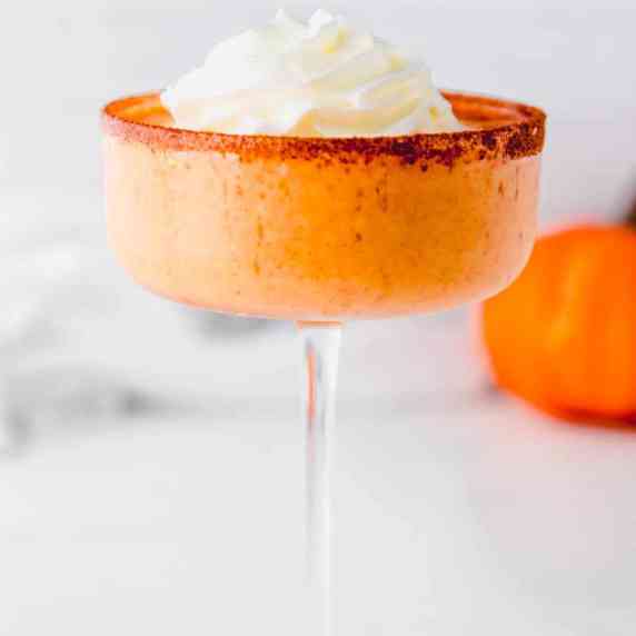 A pumpkin pie martini with frozen whipped cream garnish in a coupe glass with a cinnamon sugar rim.