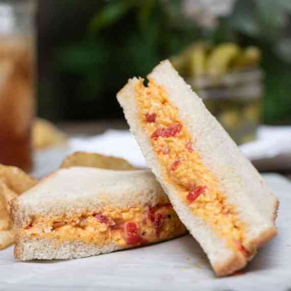A pimento cheese sandwich cut in half and served outdoors with sweet tea.