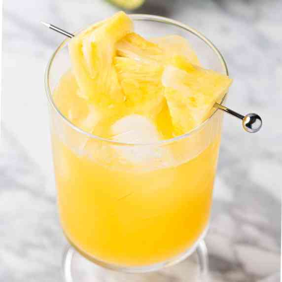 A pineapple gin cocktail garnished with pineapple chunks.