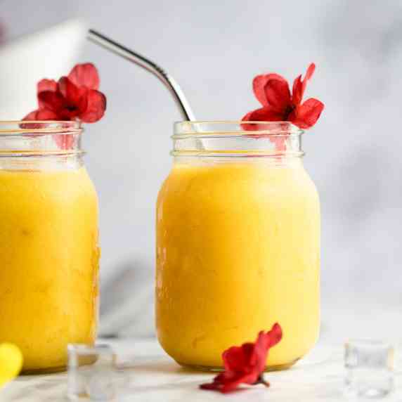 A pineapple mango smoothie in a glass jar, with a red flower on the rim of the glass.