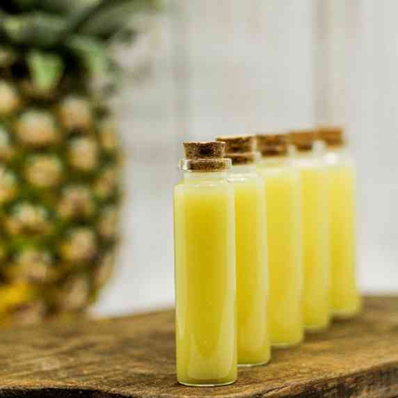 Pineapple Coconut Lemon Ginger Juice Wellness Shots in tiny glass vials on a wooden board.