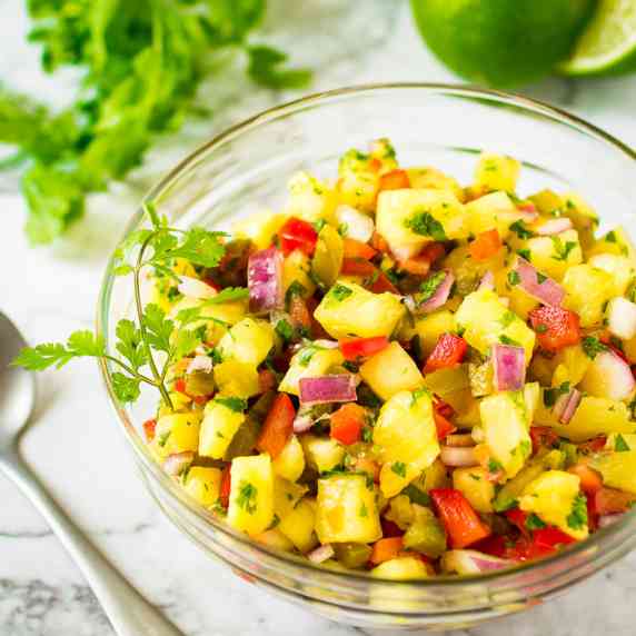 Overhead shot of pineapple salsa garnished with cilantro in a clear bowl on a white surface.