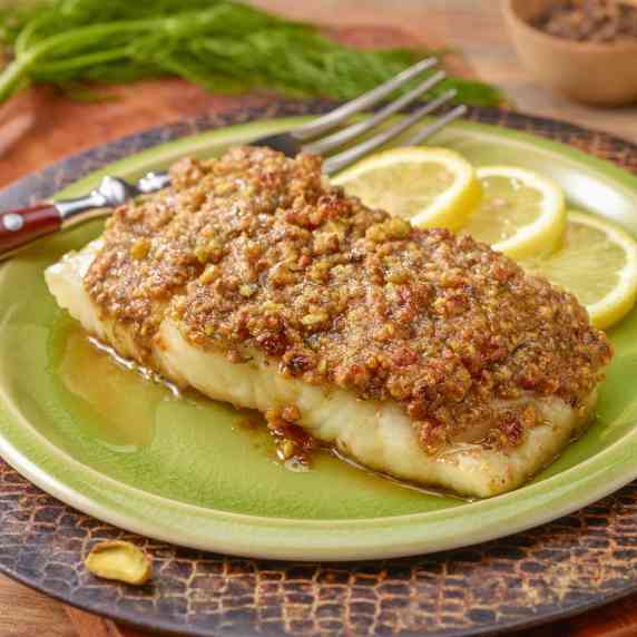 A single serving of Pistachio Crusted Fish, sitting on a light green plate that's on a cutting board