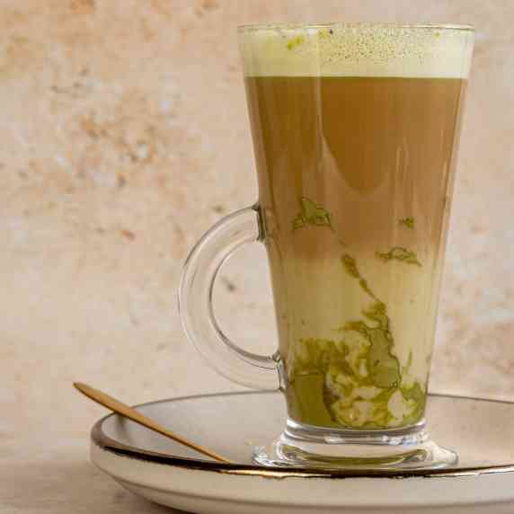 a latte glass is filled with pistachio latte with a spoon on the side